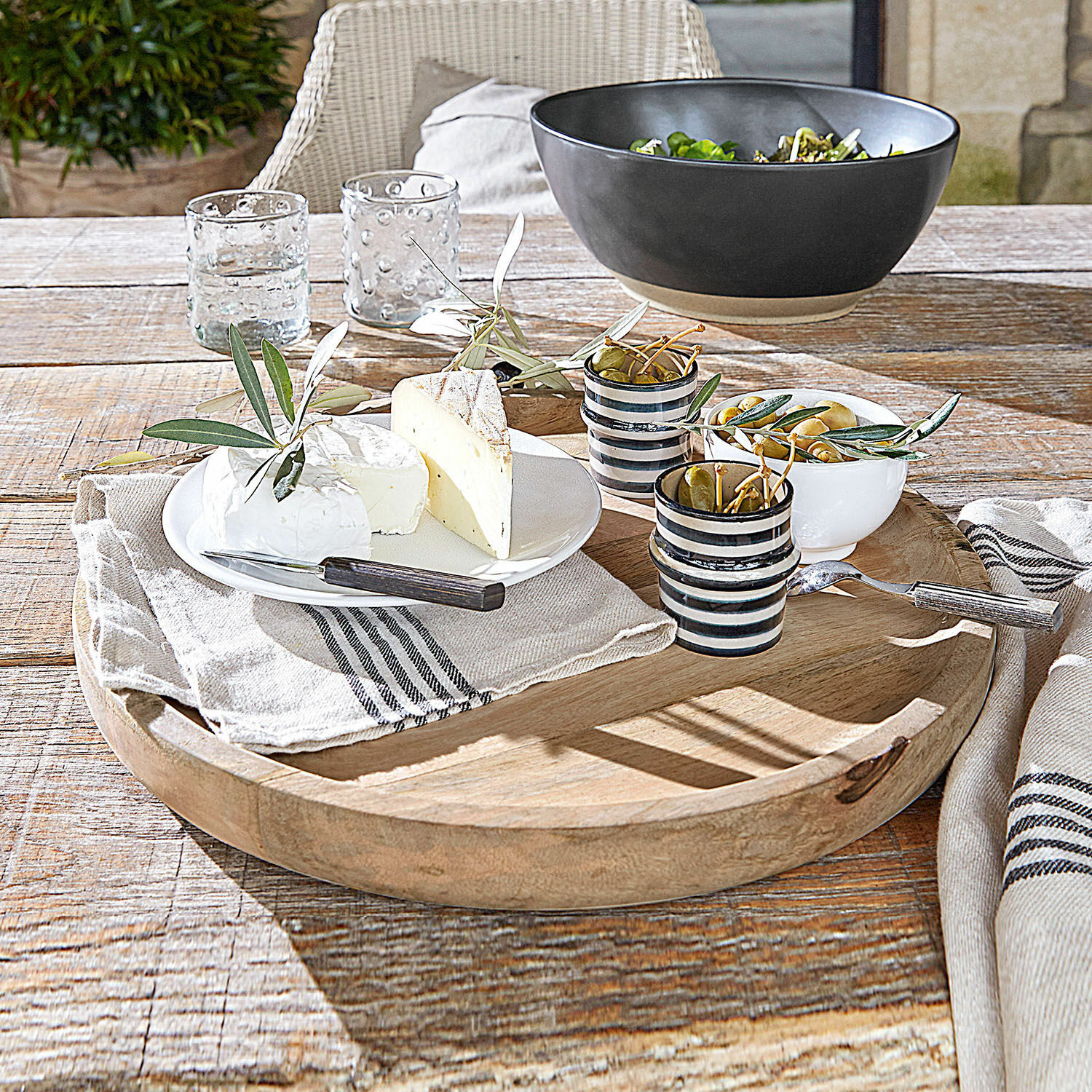 Houten dienblad met kaas, olijven en keramische bekers op rustieke houten tafel