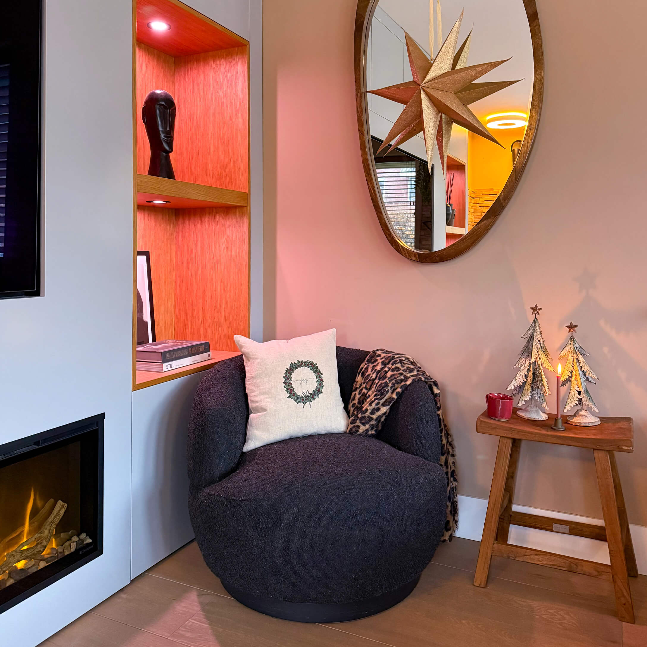 Fauteuil noir moelleux avec coussin et plaid près d'une cheminée et d'une table en bois décorée pour Noël