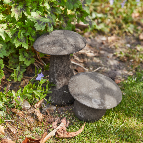 Champignons décoratifs en béton gris dans un jardin avec herbe et plantes vertes