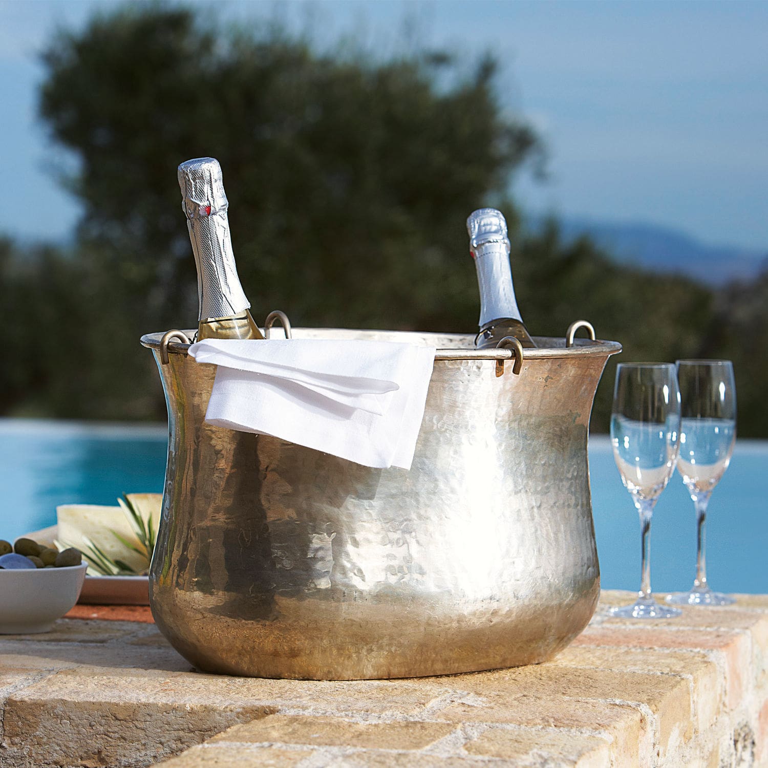 Champagnekoeler Montgomery Hamerslag koperen ijsemmer met twee champagneflessen en wit servet op terras