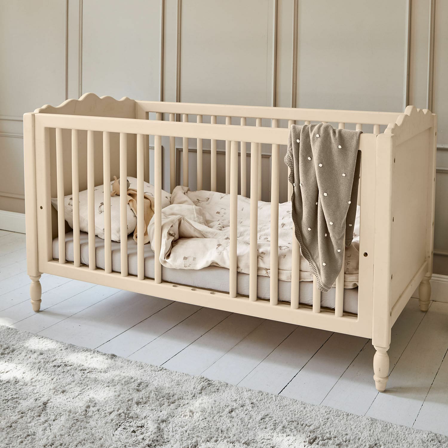 Lit bébé Arlithia Lit bébé en bois beige avec literie et couverture grise dans une chambre d'enfant lumineuse