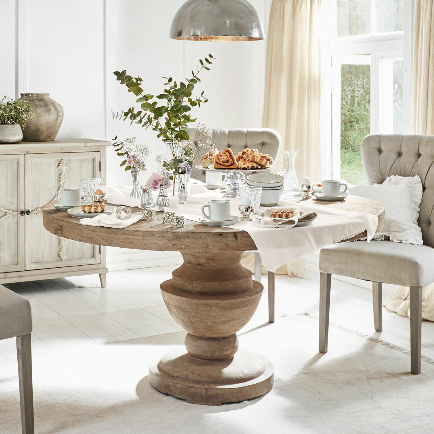 Tafel Retonfey Ronde houten tafel met decoraties en lichte stoelen in een lichte, gezellige eetkamer