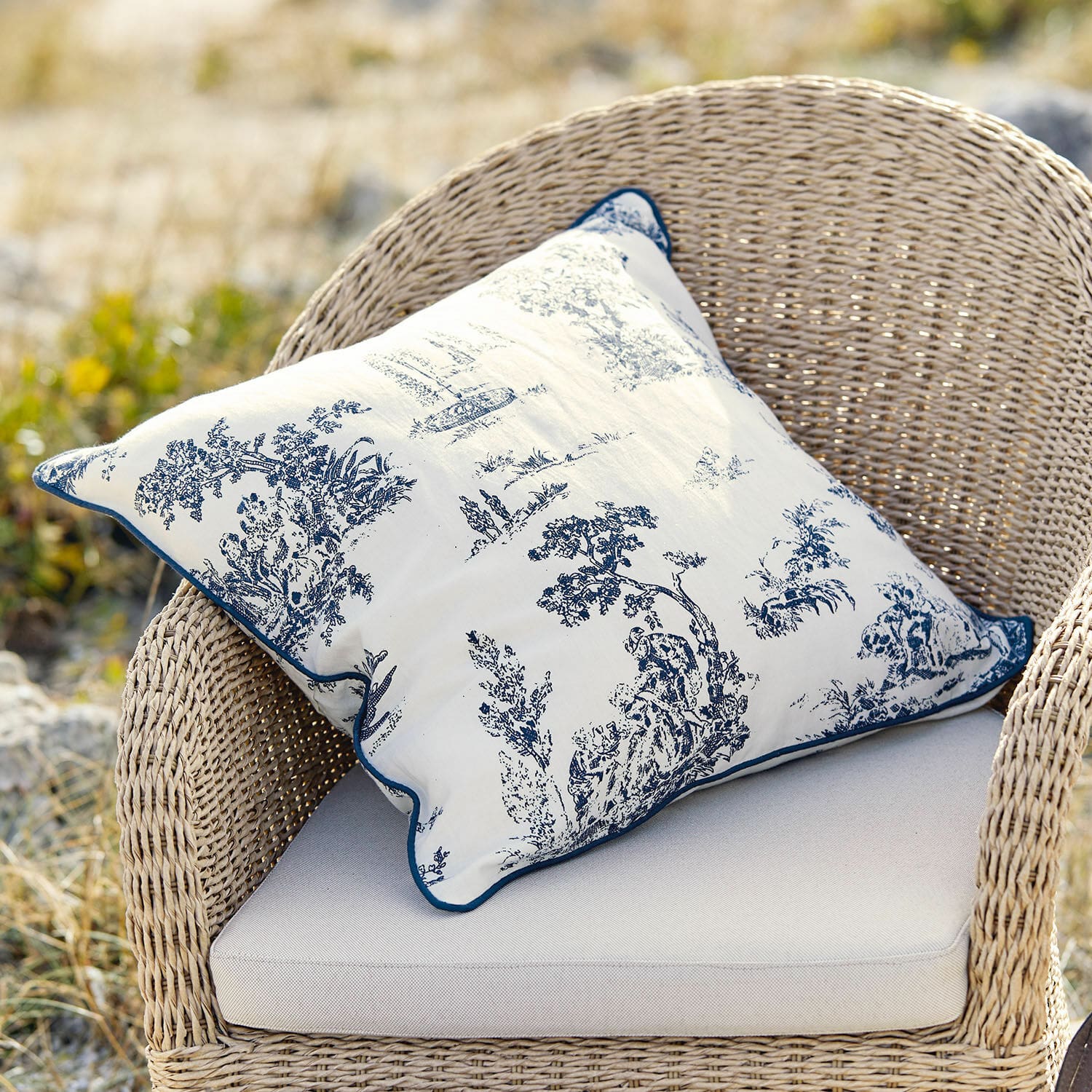 Coussin décoratif en coton blanc avec motif bleu classique sur fauteuil en osier beige