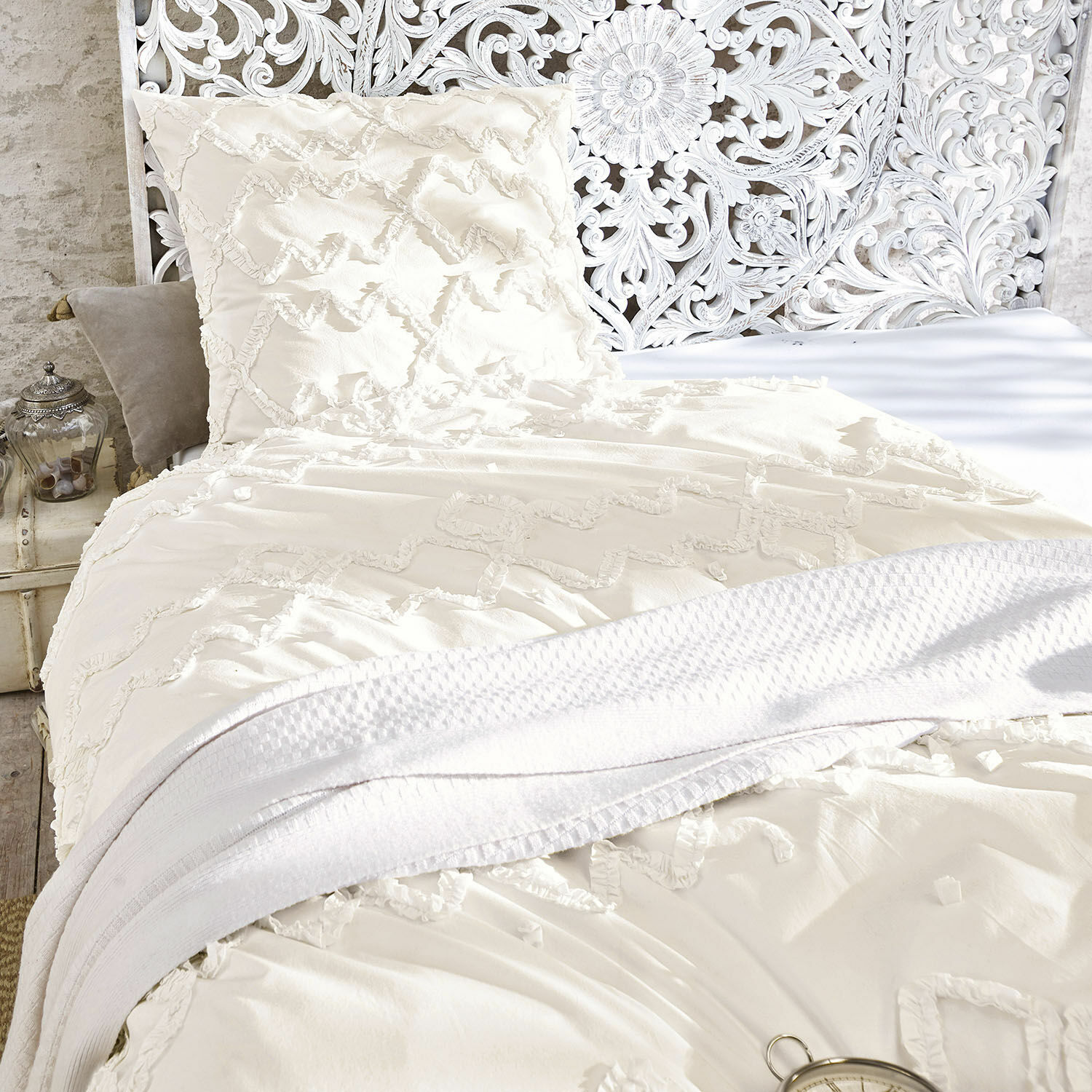 Parure de lit Élaine Parure de lit en coton crème avec motif décoratif et couverture blanche douce sur un lit vintage