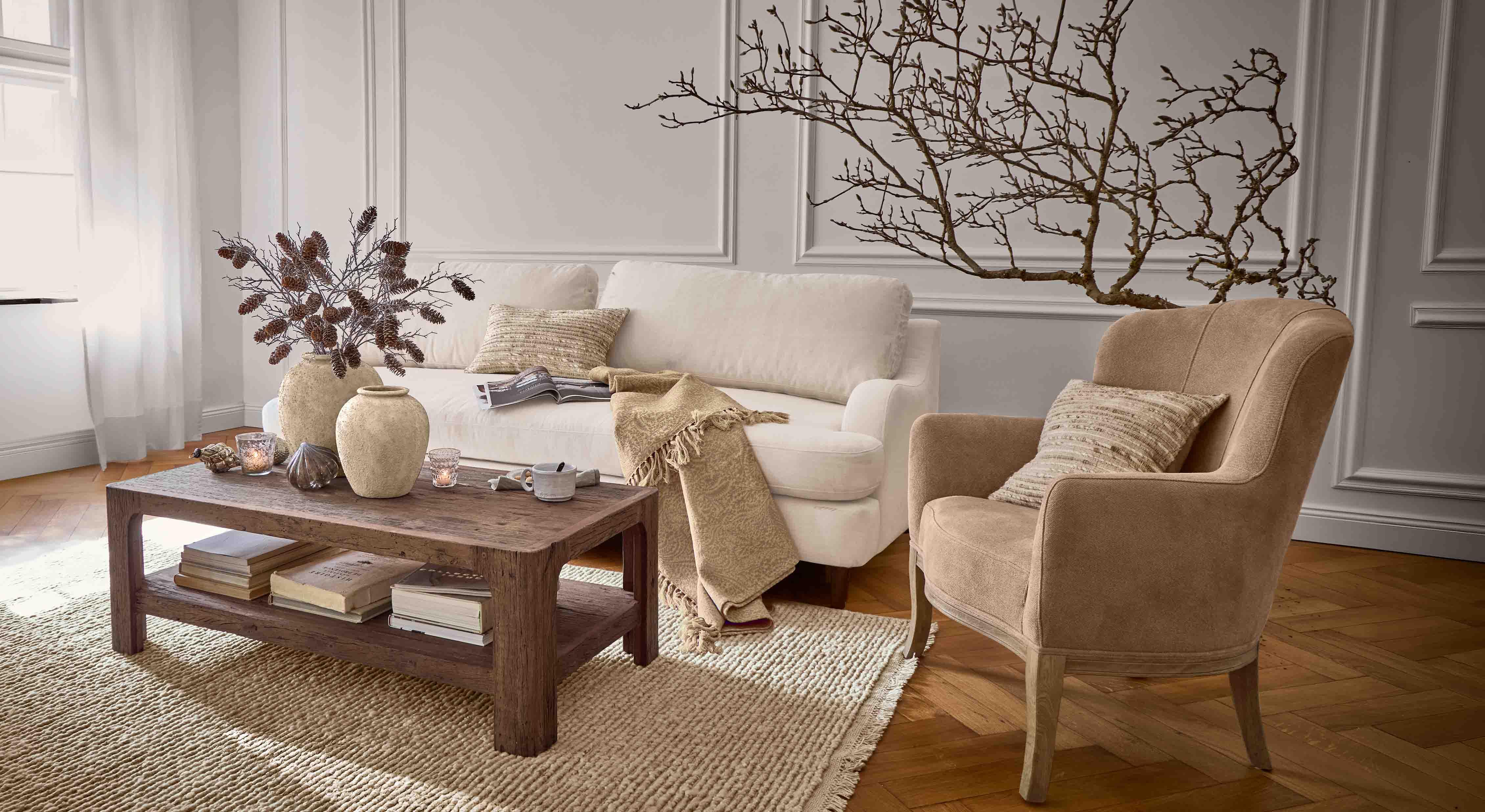 Salon chaleureux avec canapé beige, fauteuil marron et table basse en bois sur tapis tissé