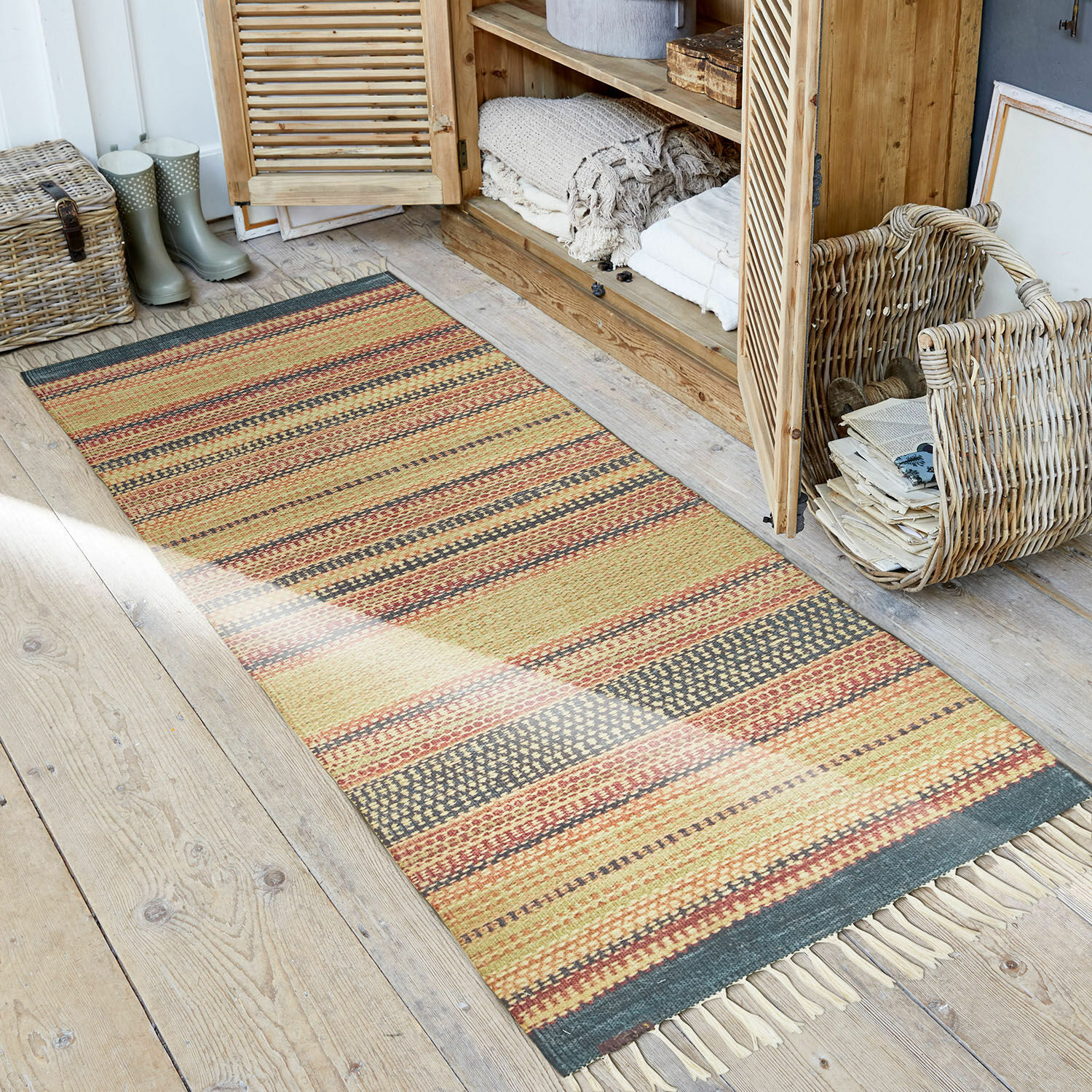 Tapis d’extérieur et d’intérieur Atlanta Tapis rayé aux tons chauds avec franges sur un sol en bois dans un intérieur rustique