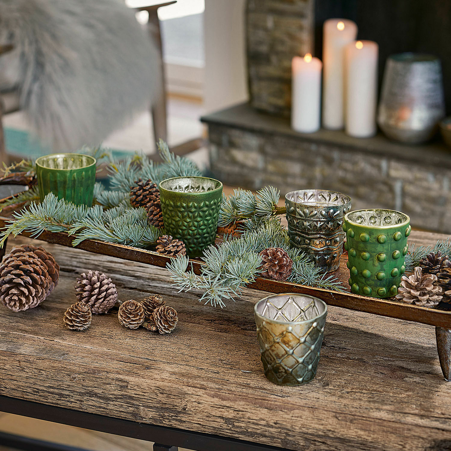 Lot de 5 photophores Morazan Photophores en verre vert et argenté avec branches et pommes de pin sur une table en bois rustique