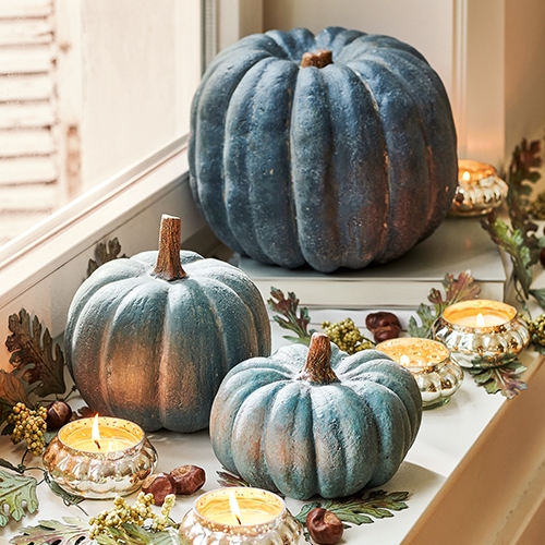 Decoratieve blauwe pompoenen op vensterbank met brandende kaarsen en herfstbladeren