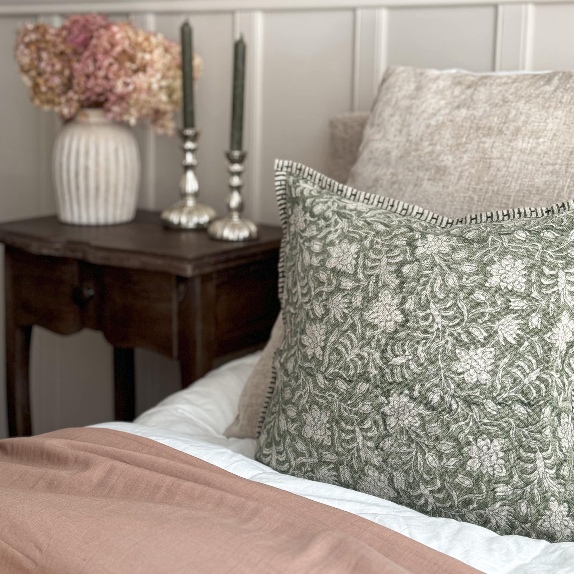 Coussin décoratif vert à motif floral sur tissu beige posé sur un lit dans un intérieur vintage