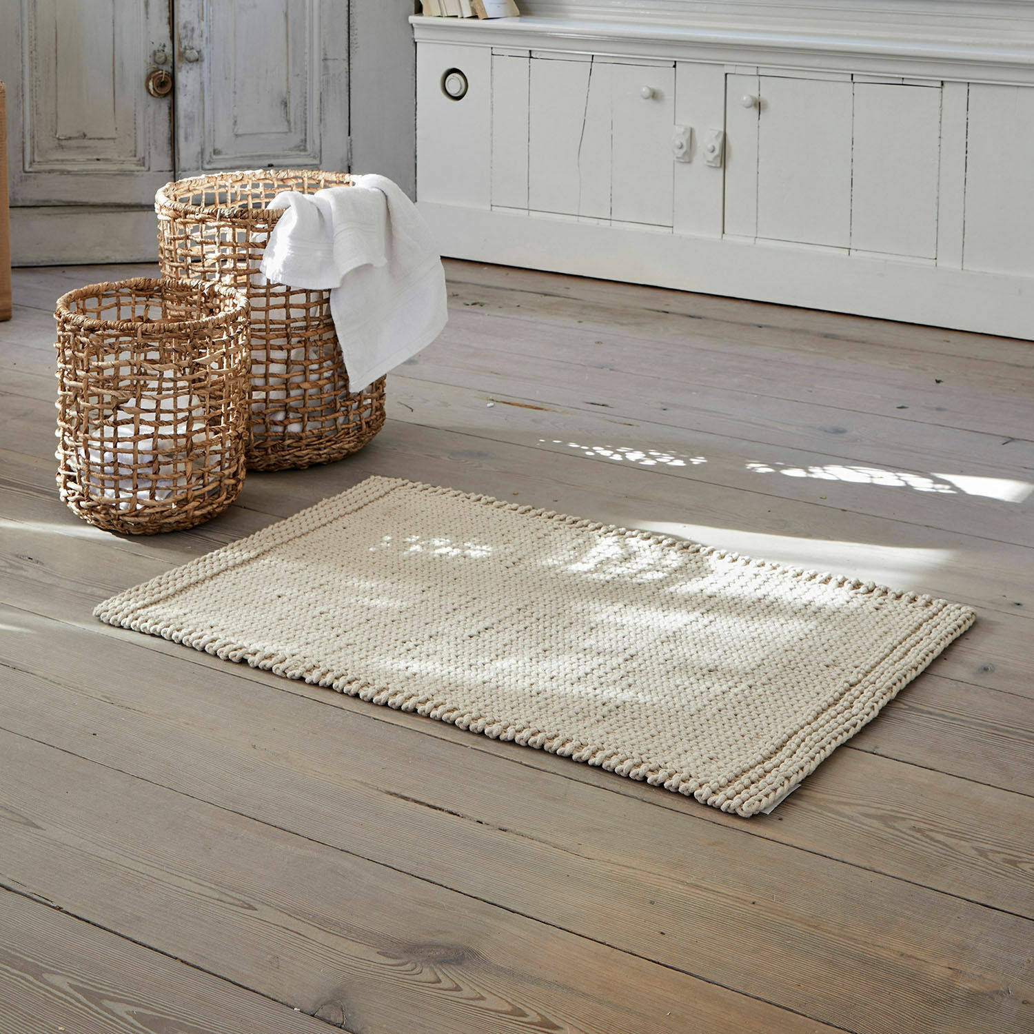 Badmat Carsen Beige katoenen vloerkleed op houten vloer met rieten opbergmanden