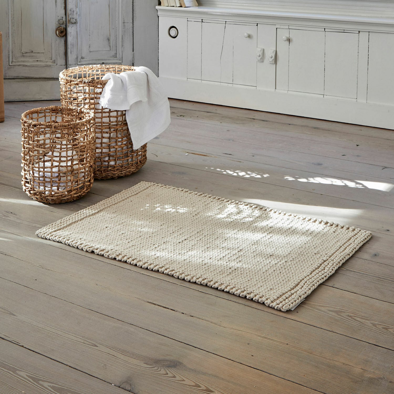 Badmat Carsen Beige katoenen vloerkleed op houten vloer met rieten opbergmanden