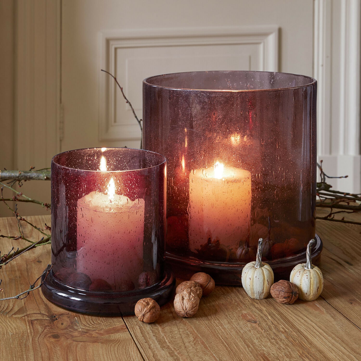 Lot de 2 photophores Saffrone Deux bougies allumées dans des photophores en verre violet sur une table en bois avec décorations d'automne