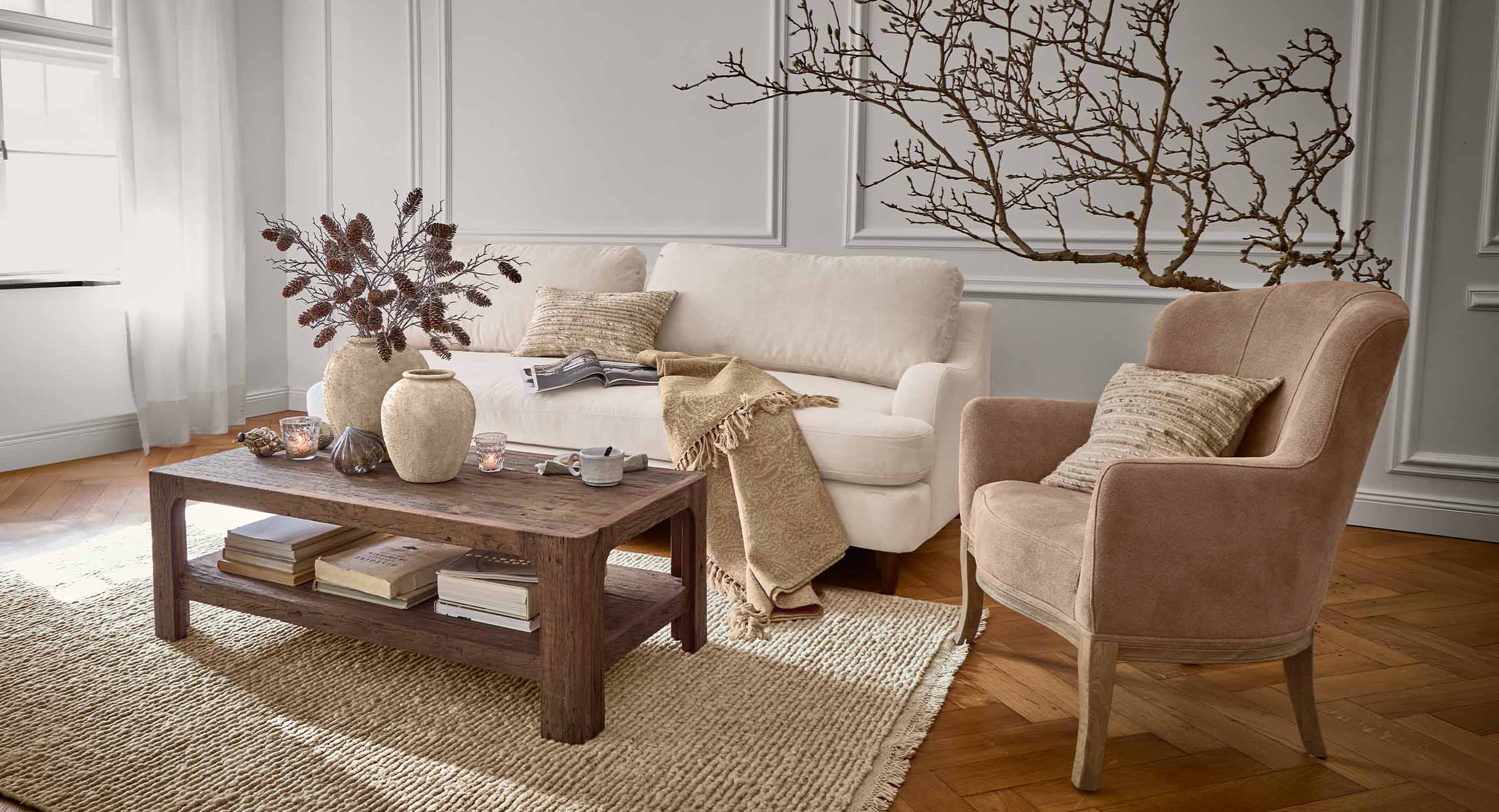 Gezellige woonkamer met beige bank, bruine fauteuil en houten salontafel op een vloerkleed van natuurlijke vezels