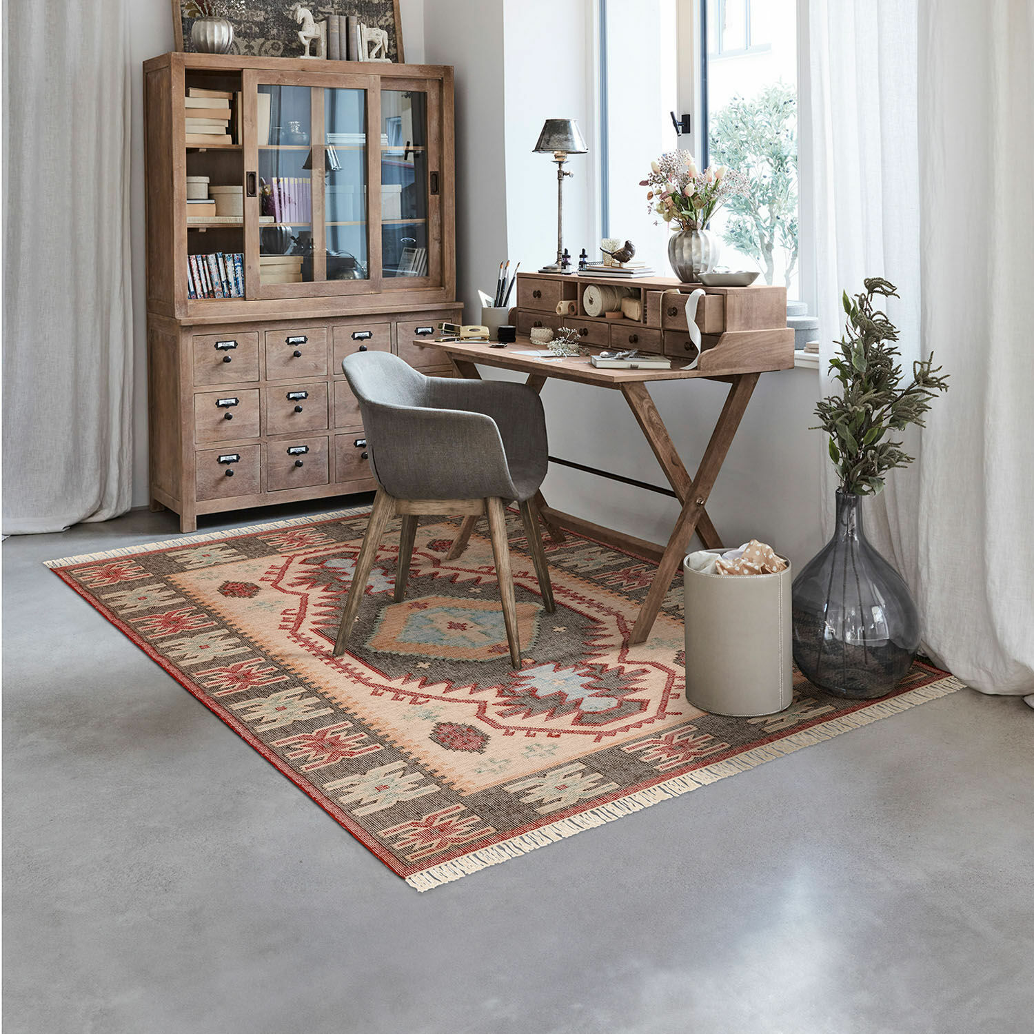 Tapis Frída Bureau chaleureux avec bureau en bois et chaise grise sur tapis coloré à motifs ethniques