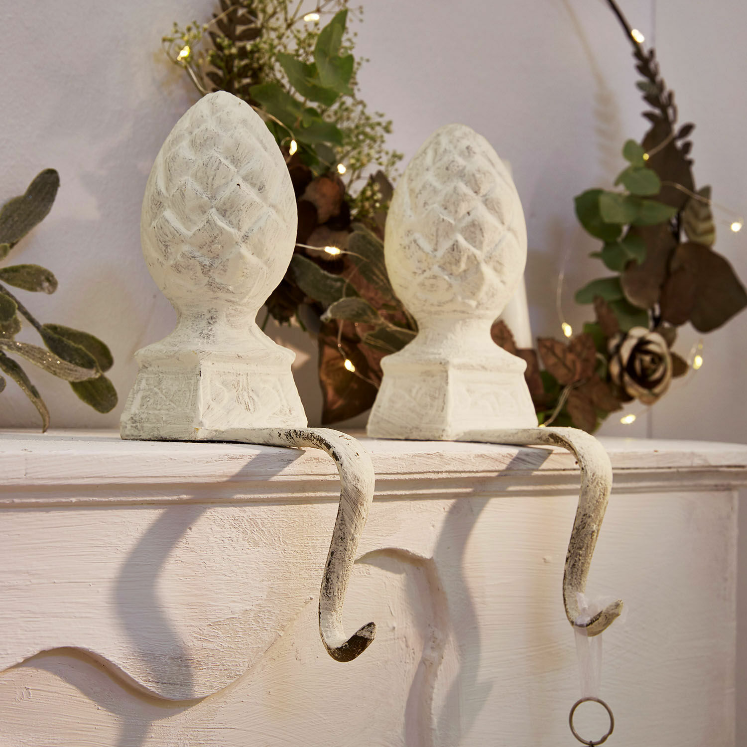 Set van twee witte metalen haken met dennenappelvormige decoratie voor het ophangen van versieringen