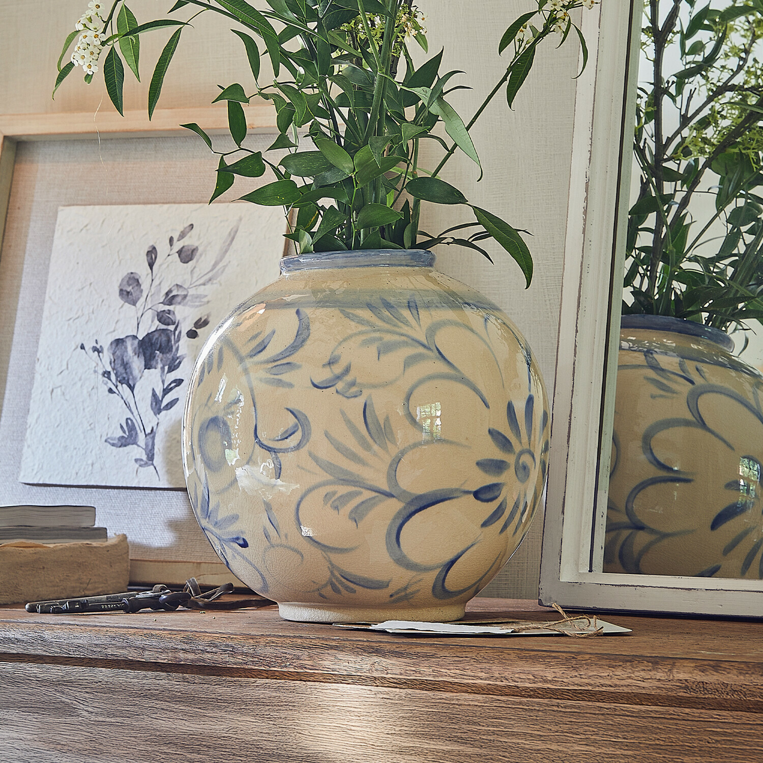 Vaas Oviren Ronde keramische vaas beige met blauw bloemmotief op houten tafel met groene bladeren
