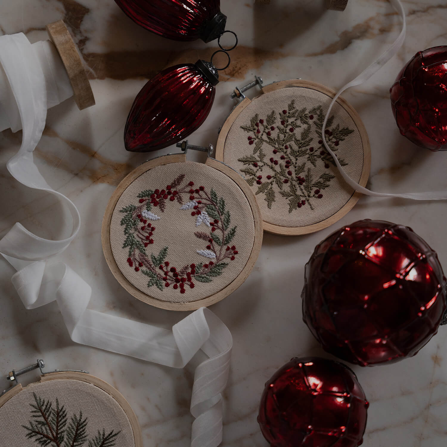 Décorations de Noël avec broderies végétales sur toile beige et boules rouges brillantes