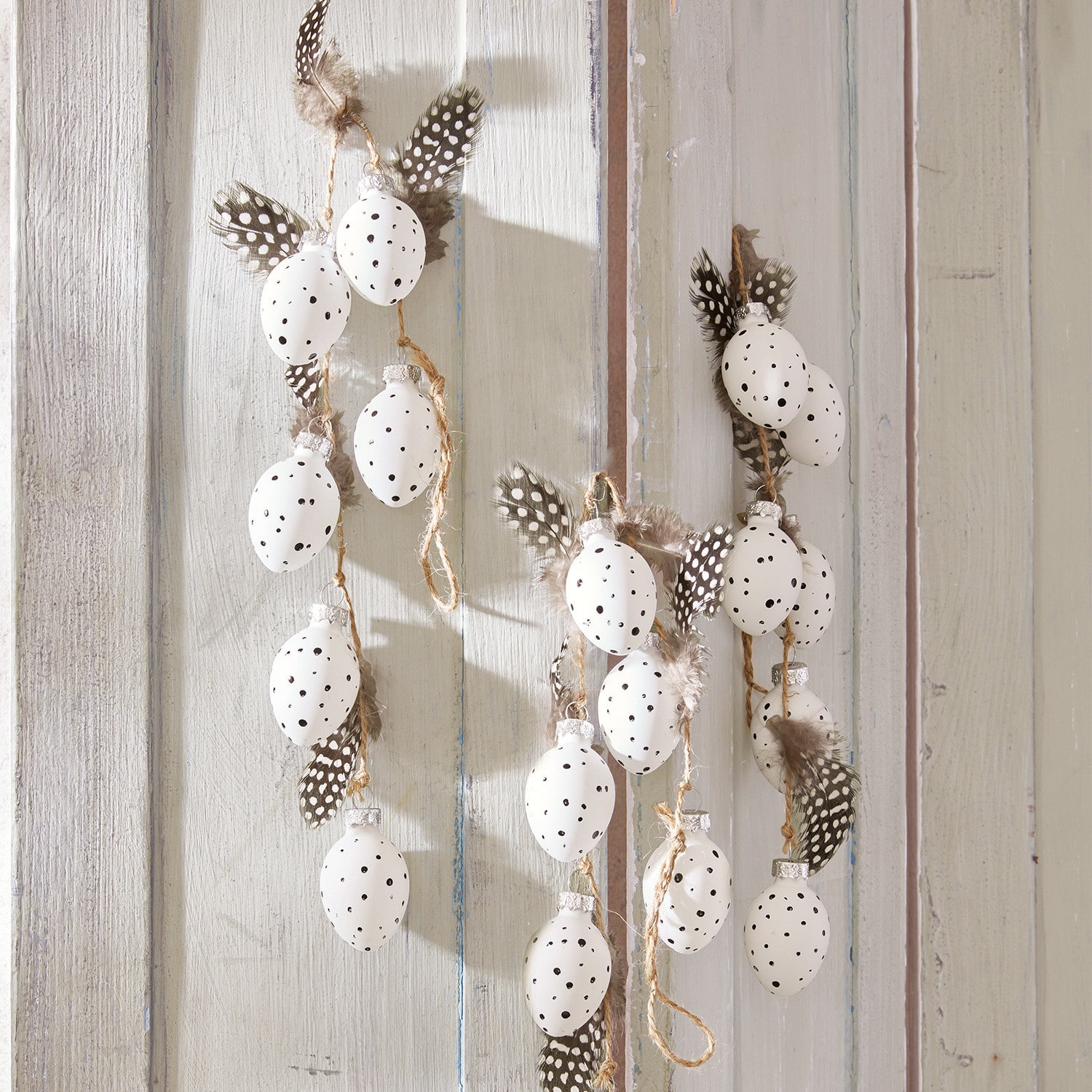 Lot de 3 guirlandes Prina Guirlande décorative avec œufs blancs à pois noirs et plumes sur fond bois clair, décoration printanière