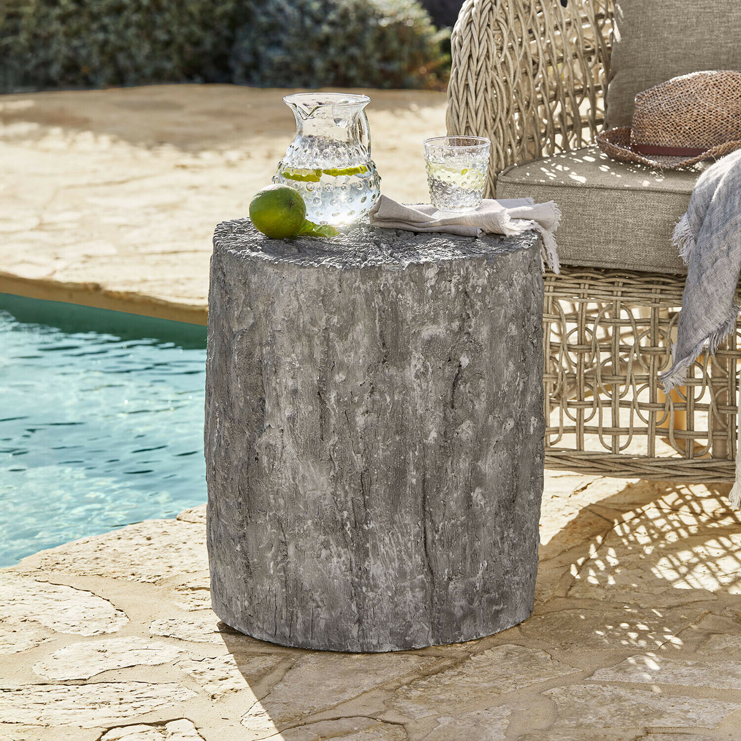 Table d’appoint Falmont Table d'appoint grise en béton à texture bois près d'un fauteuil en osier au bord de la piscine