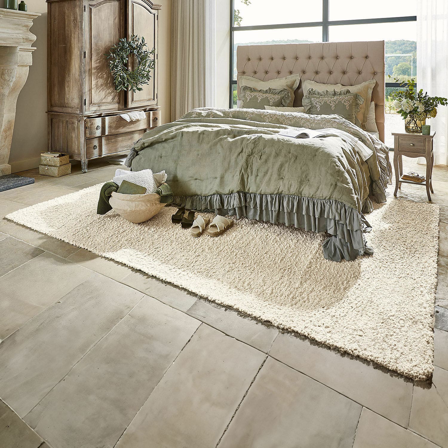 Tapis Wodaha Chambre chaleureuse avec lit capitonné beige et linge de lit vert sur tapis crème sur sol en pierre
