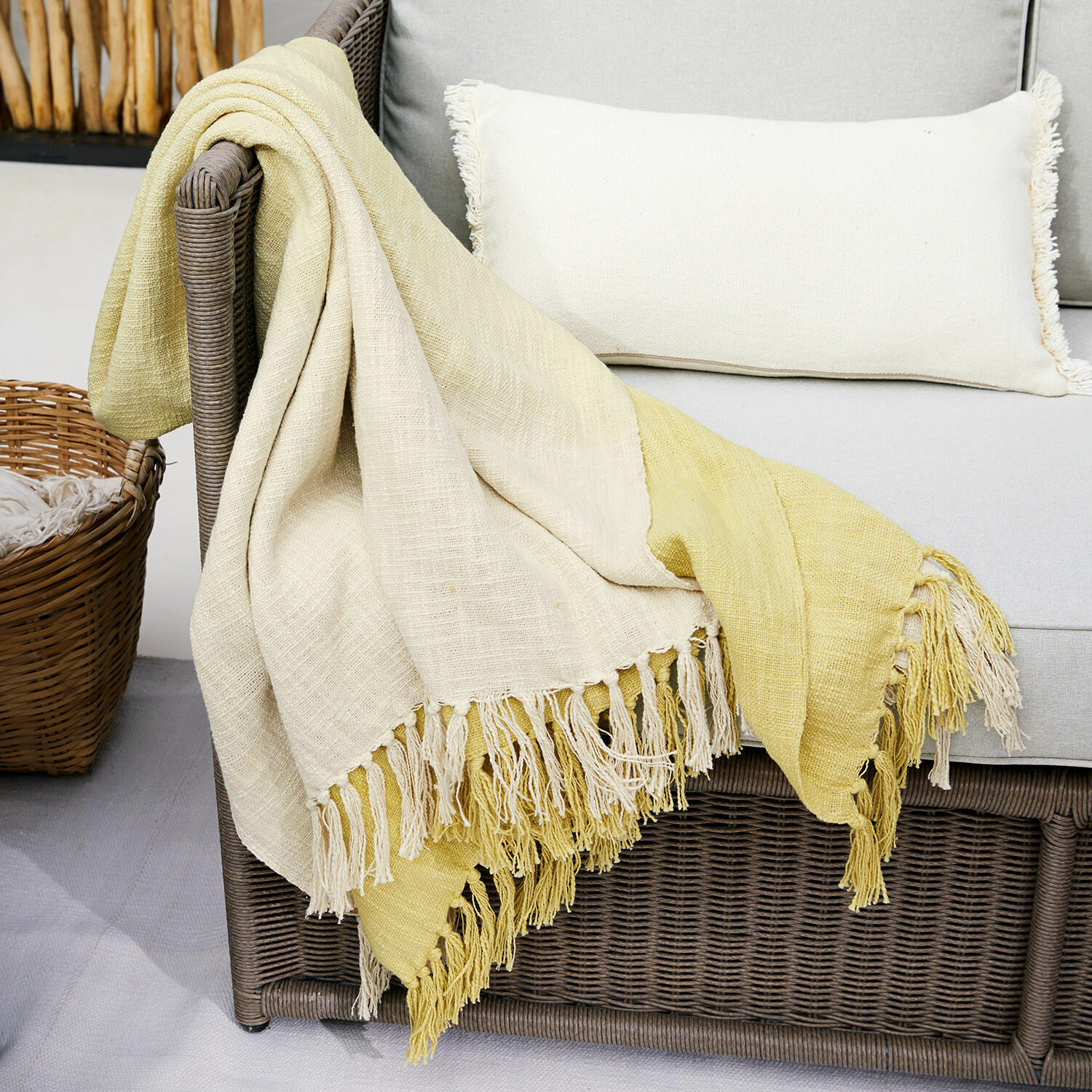 Plaid Aurice Plaid bicolore en coton crème et jaune avec franges sur canapé en osier gris