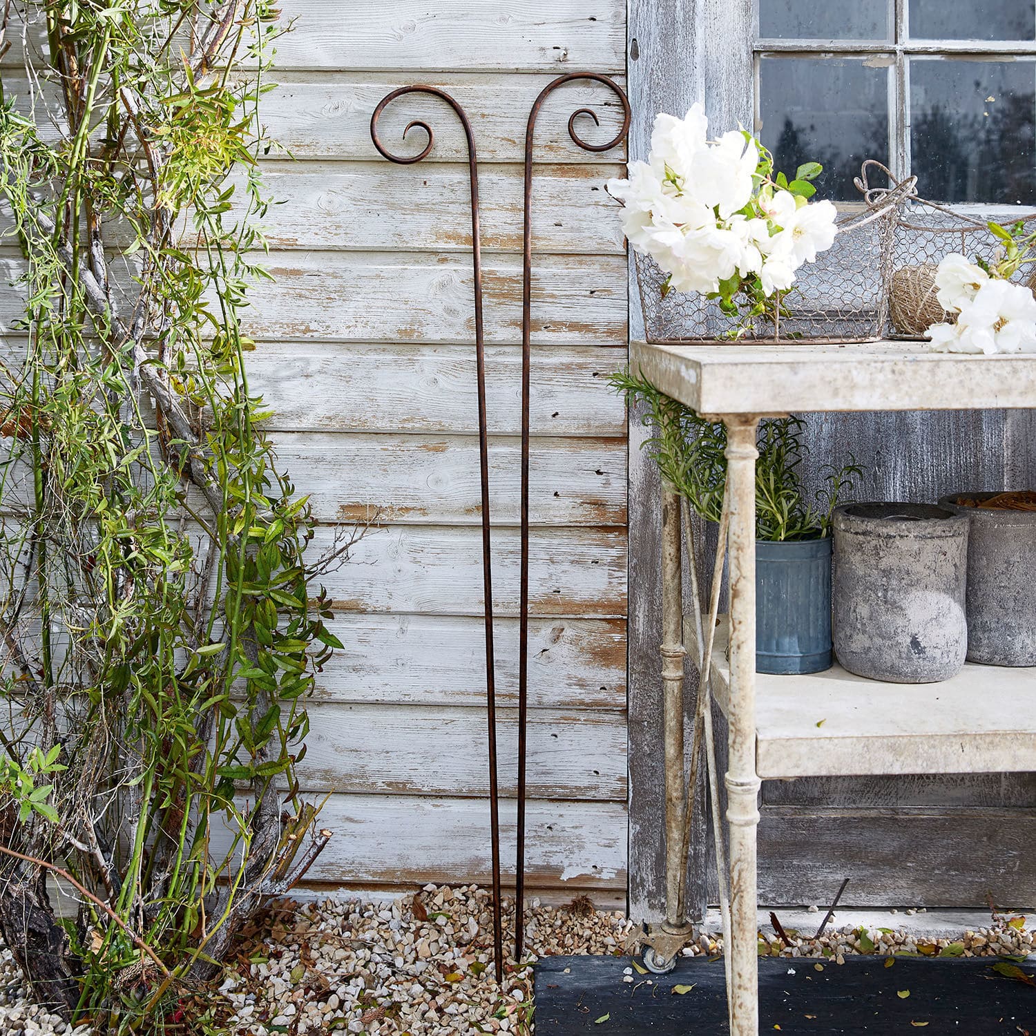Lot de 2 piques de jardin Dorhal Support de plante en métal rouillé au style rustique contre un mur en bois blanc extérieur