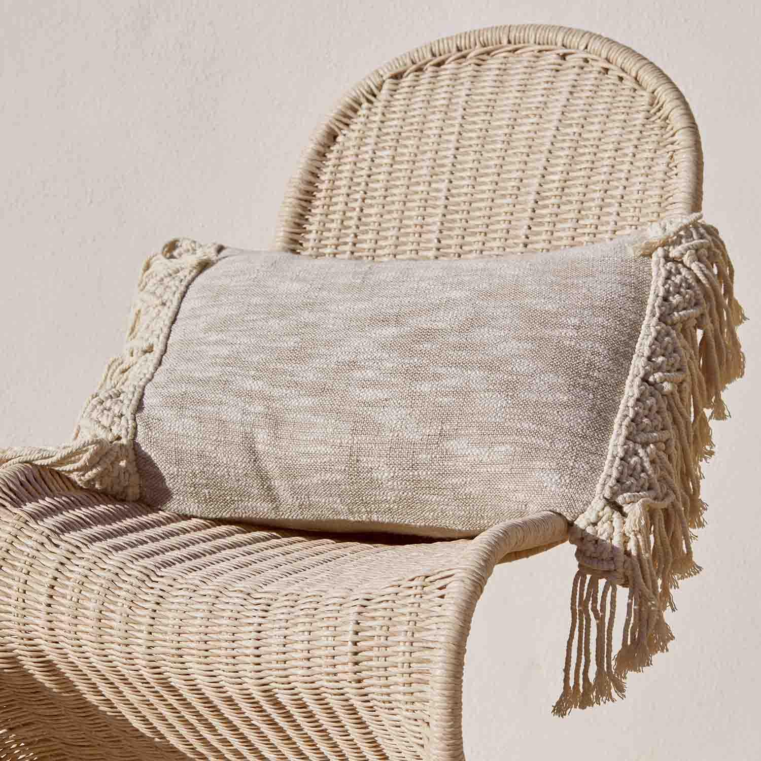 Beige sierkussen met franjes op een rotan stoel, natuurlijk materiaal, boho stijl